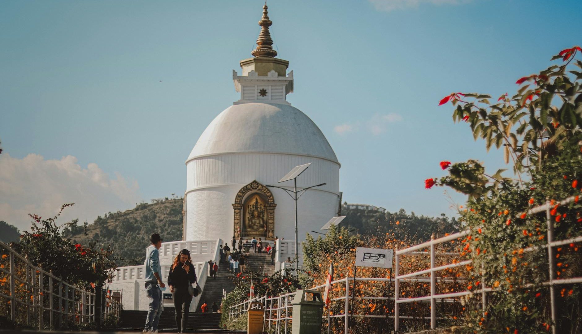 Tourists walking near the World Peace Pagoda surrounded by flowers in Nepal.